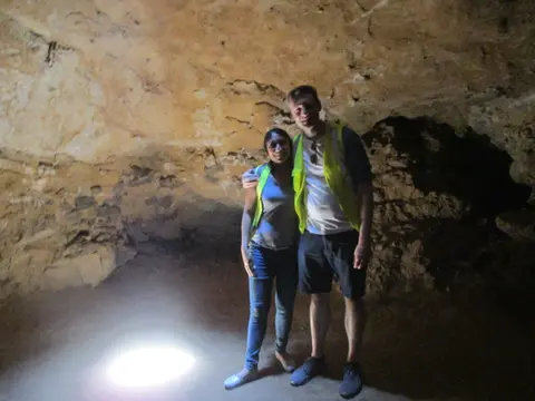 Dos personas posan juntas en una cueva oscura con luz brillante.