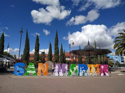 Letrero gigante de SAN MIGUEL, con árboles altos y un cielo azul con nubes.