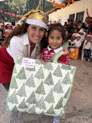 Mujer y niña sonriendo sosteniendo regalo con árboles verdes. Galeria. Navidad en la comunidad.