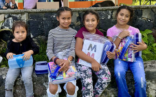 Niñas sonriendo muestran útiles escolares con la letra M en frente. TUSUEÑO.COM