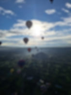 Globos aerostáticos flotan sobre el paisaje, cielo azul y sol brillando intensamente.