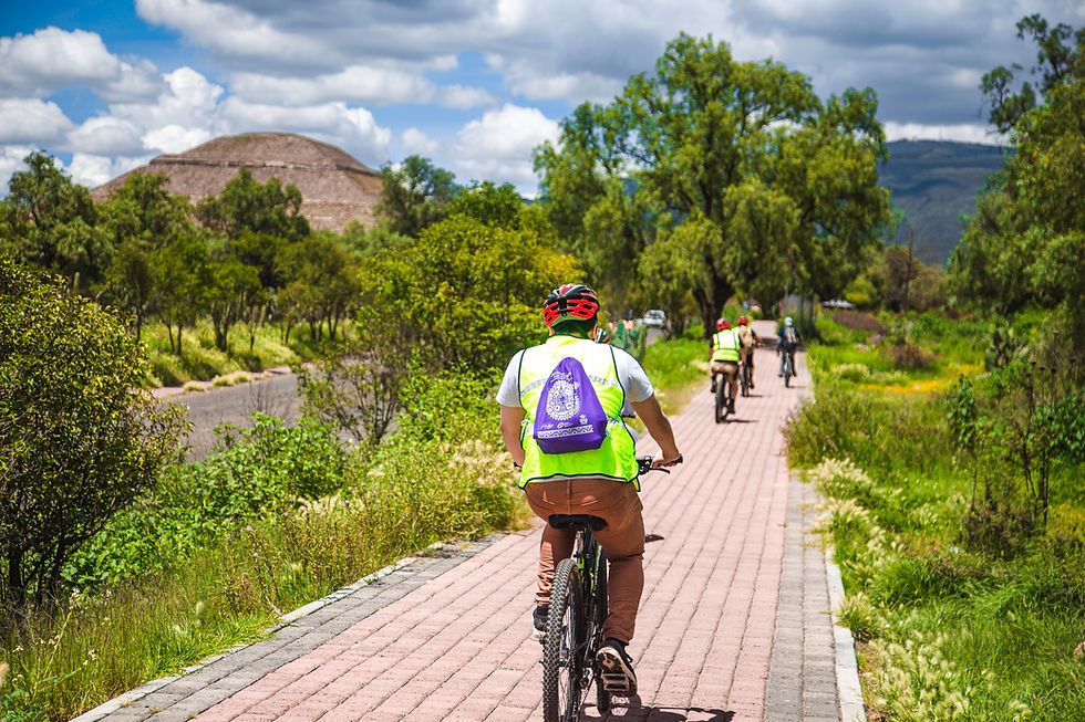 Ciclistas recorren sendero con pirámide y árboles rodeando en un día soleado.