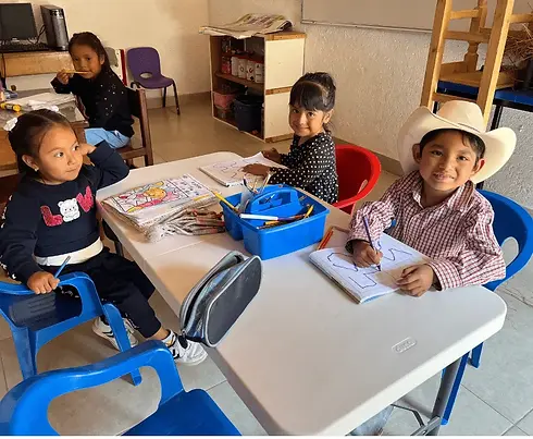Niños sonriendo en clase, escribiendo en cuadernos y aprendiendo juntos.