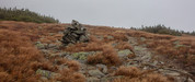 Rock cairn marking a windswept pass at Edmands Col in New Hampshire’s White Mountains, surrounded by golden alpine grasses, scattered boulders and misty mountain peaks.