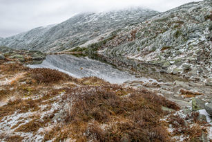 Snow-dusted rocks and still reflective water at Lakes of the Clouds on Mount Washington in early winter.