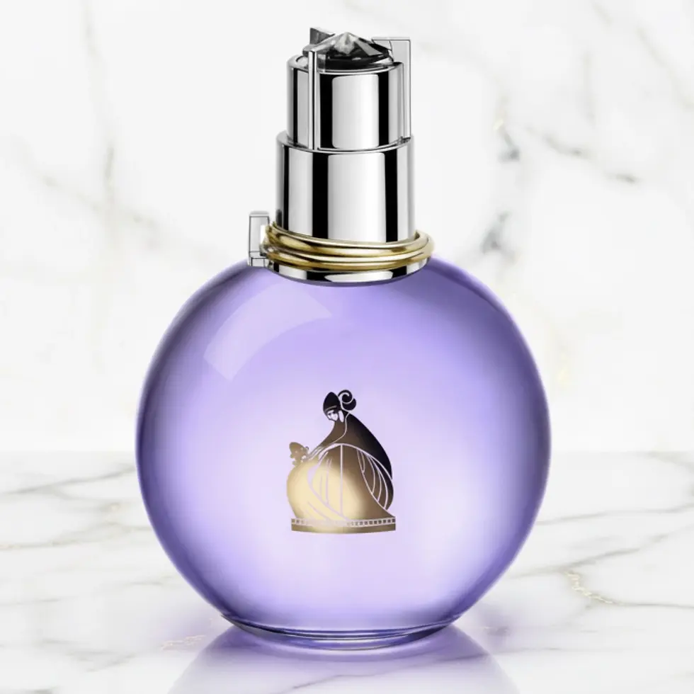 Flacon de parfum sphérique violet avec un motif doré sur un fond de marbre blanc.