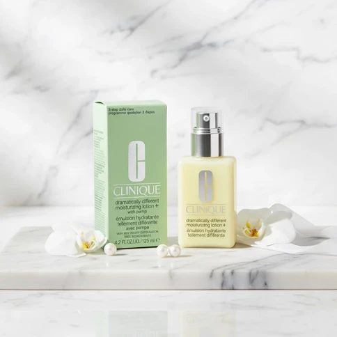 Flacon de lotion jaune, boîte verte, orchidées blanches et perles sur marbre.