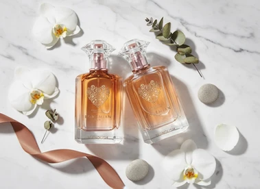 Deux flacons de parfum ambré entourés d'orchidées blanches, de galets et d'un ruban cuivré.