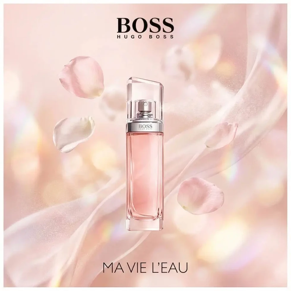 Flacon Boss Ma Vie L'Eau entouré de pétales roses flottants sur fond rose poudré