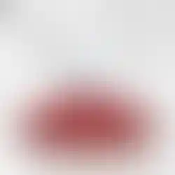 Flacon de parfum rouge en forme d'amande sur fond de marbre blanc et gris.