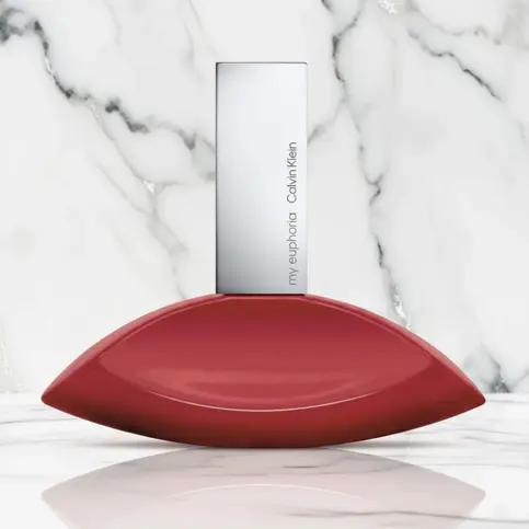 Flacon de parfum rouge en forme d'amande sur fond de marbre blanc et gris.