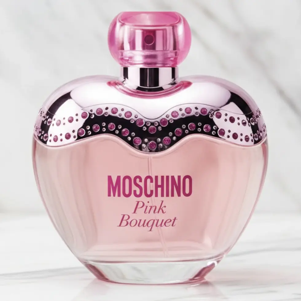 Flacon de parfum en forme de cœur rose sur marbre blanc.