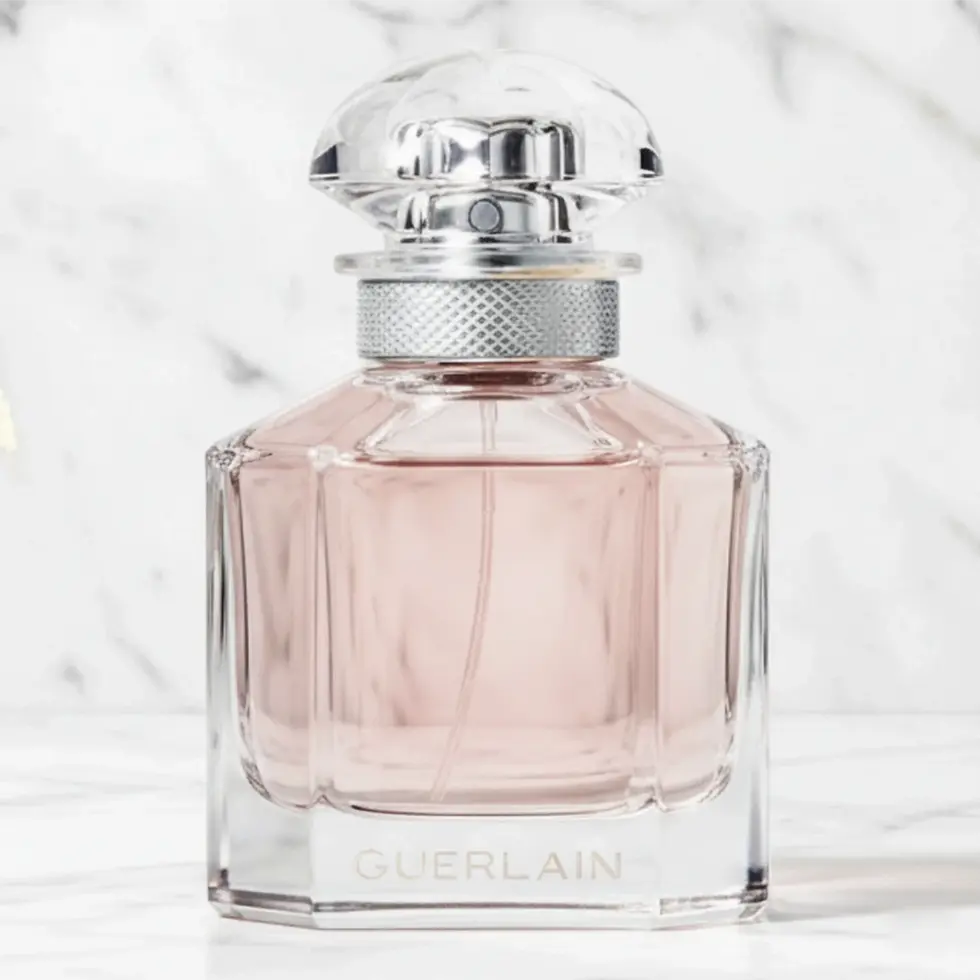 Flacon de parfum en verre rose avec un bouchon facetté sur un fond de marbre blanc.