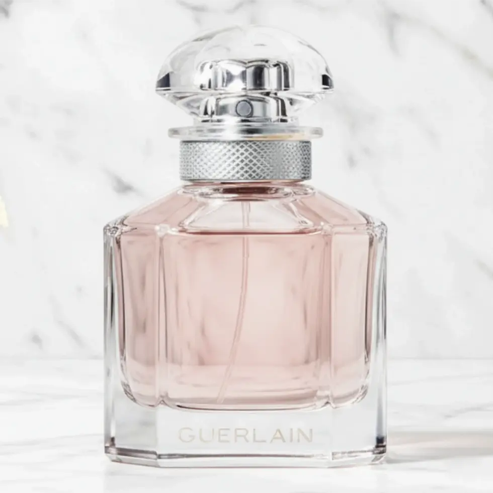 Flacon de parfum en verre rose avec un bouchon facetté sur un fond de marbre blanc.