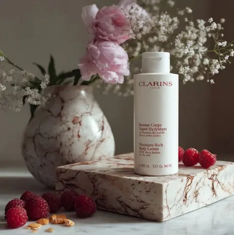 Gros plan sur la lotion corporelle Clarins, posée à côté de framboises et de fleurs roses.