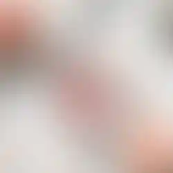 Flacon de parfum rectangulaire rose avec un cœur fleuri et une chaîne dorée, entouré de roses sur du marbre blanc.