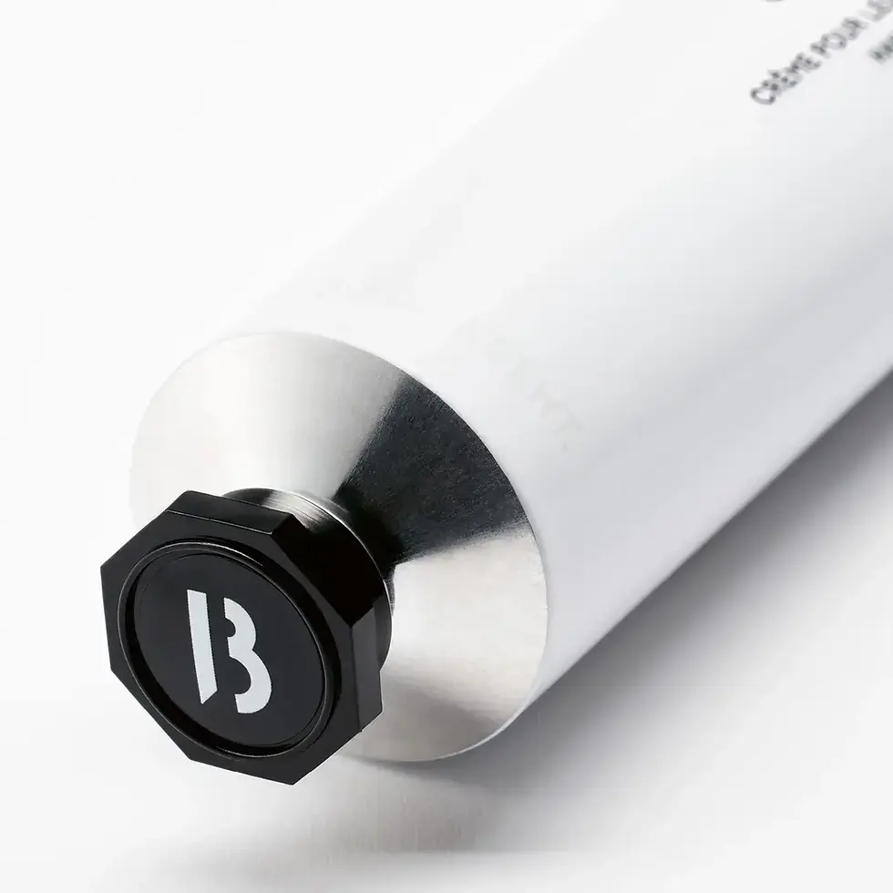 Gros plan bouchon octogonal noir logo Byredo B blanc sur tube crème mains blanc, col en acier brossé