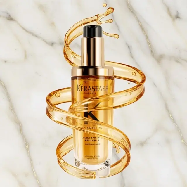 Flacon de l'huile capillaire Kérastase Elixir Ultime rechargeable, avec tourbillon d'huile dorée, sur fond marbre.