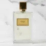 Flacon de parfum rectangulaire transparent avec étiquette dorée sur un fond de marbre blanc.