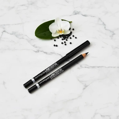 Deux crayons khôl noirs posés sur du marbre blanc, avec une fleur blanche.