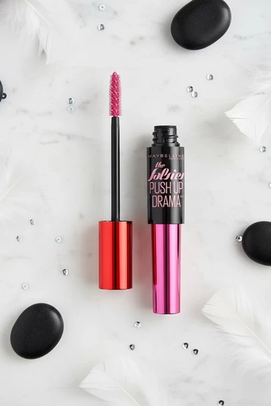 Mascara ouvert avec sa brosse à picots roses, sur du marbre blanc avec plumes et pierres.