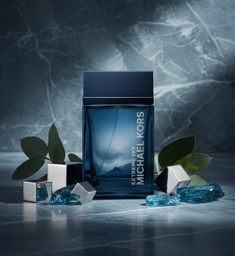 Flacon de parfum bleu marine et transparent entouré de feuilles et de cristaux bleus.