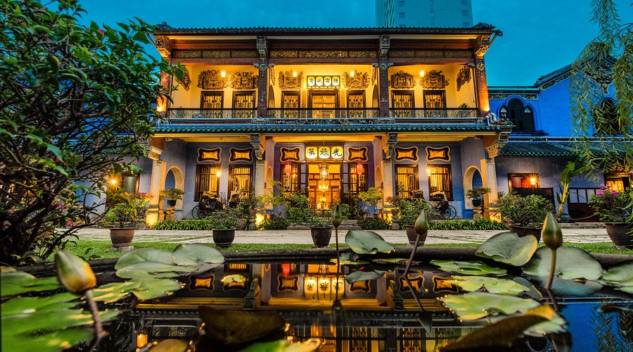 Facciata esterna di un Mansion in stile tradizionale, illuminata di sera, di fronte stagno con ninfee