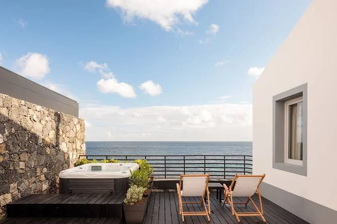 Patio esterno di una camera d'hotel con vasca idromassaggio e sdraio, vista mare