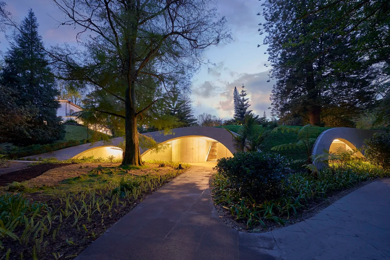 vista esterna di un giardino con elementi in cemento ad arco, illuminati durante la sera