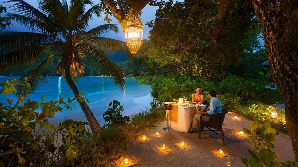 Cena romantica con candele in spiaggia in mezzo a palme e vegetazione lussureggiante