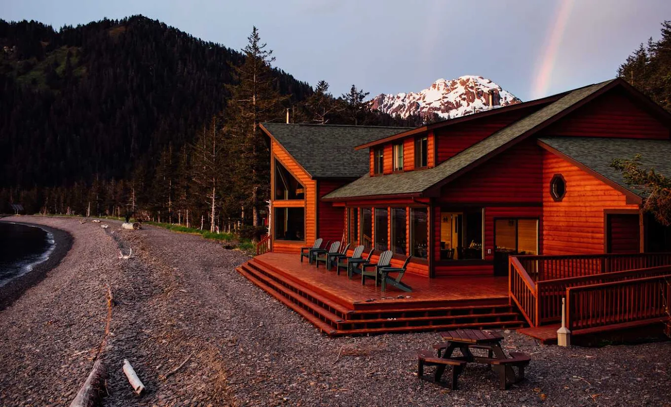 Vista esterna di un lodge in legno su una spiaggia di ciottoli e sullo sfondo montagne
