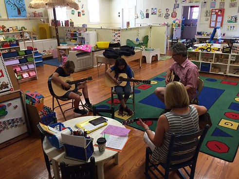 4 people sitting in colorful classroom playing guitars