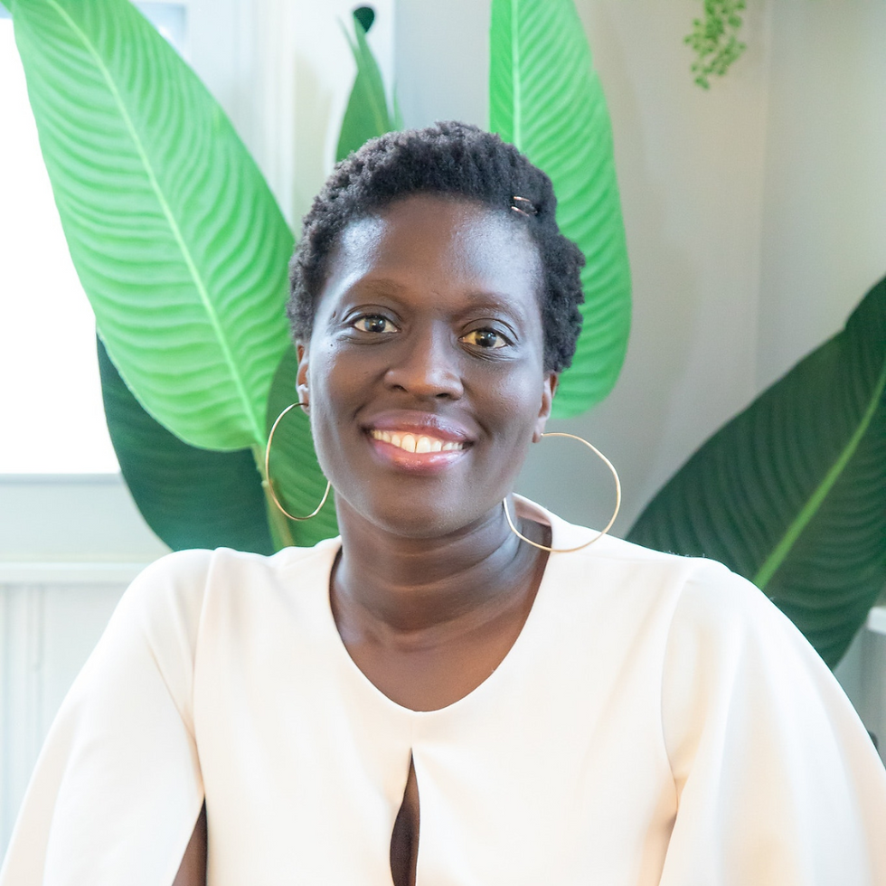 Smiling woman in a white top and hoop earrings posed indoors against oversized green leaves.