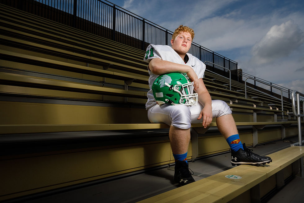 A high school senior football player sits in the stands of his home stadium.