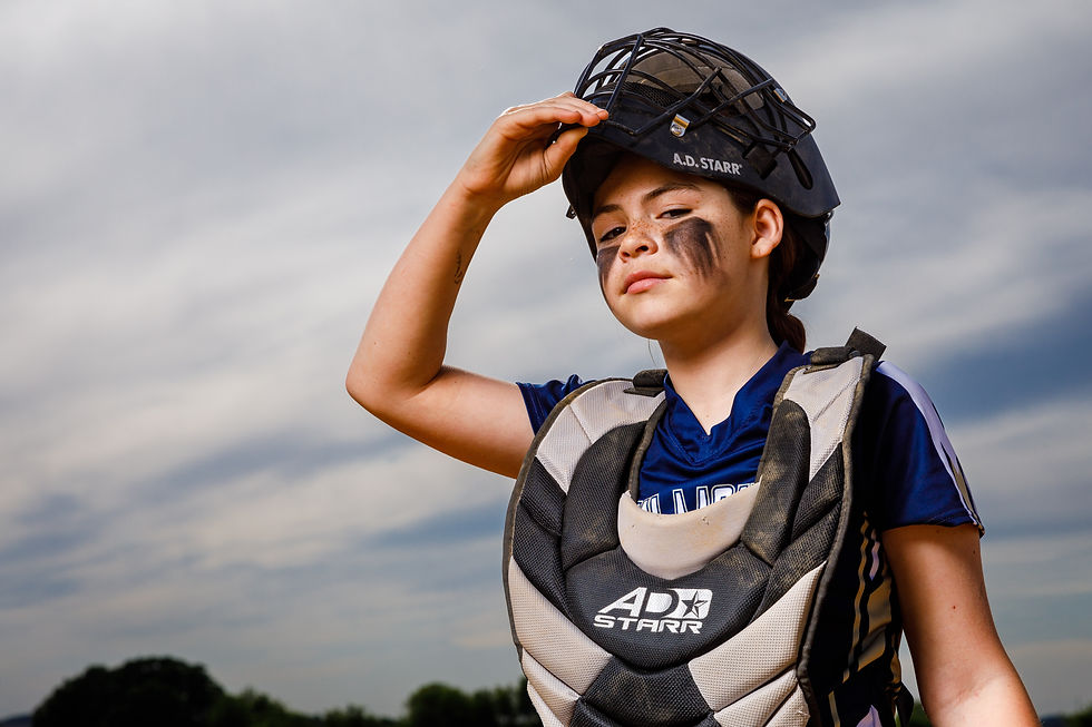 A youth softball catcher lifts up her mask.