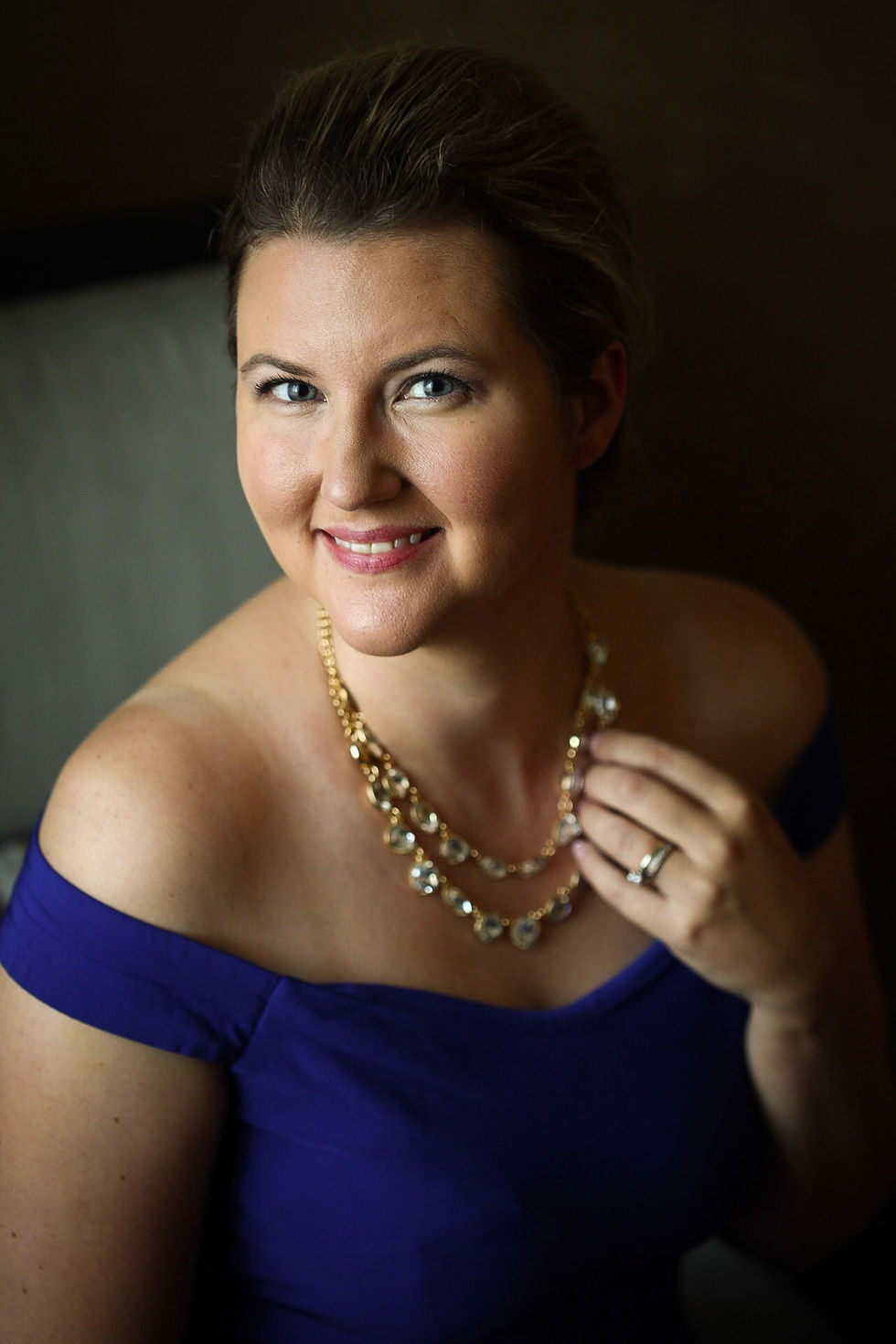 A woman touches her necklace in a window light portrait.