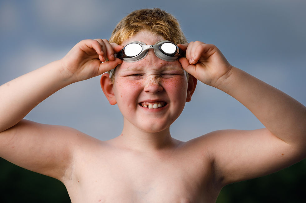 A youth swimmer holds his goggles and smiles.