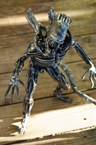 A toy xenomorph from the film Alien standing on wood.