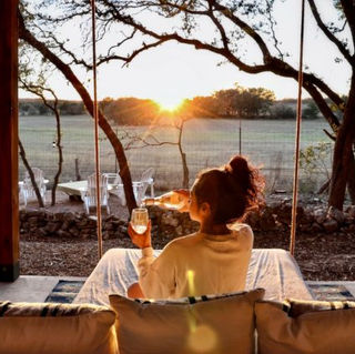 The Lazy Lavender Treehouse in Wimberley Texas — Woman on Swinging Daybed at Golden Hour with Hill Country Views