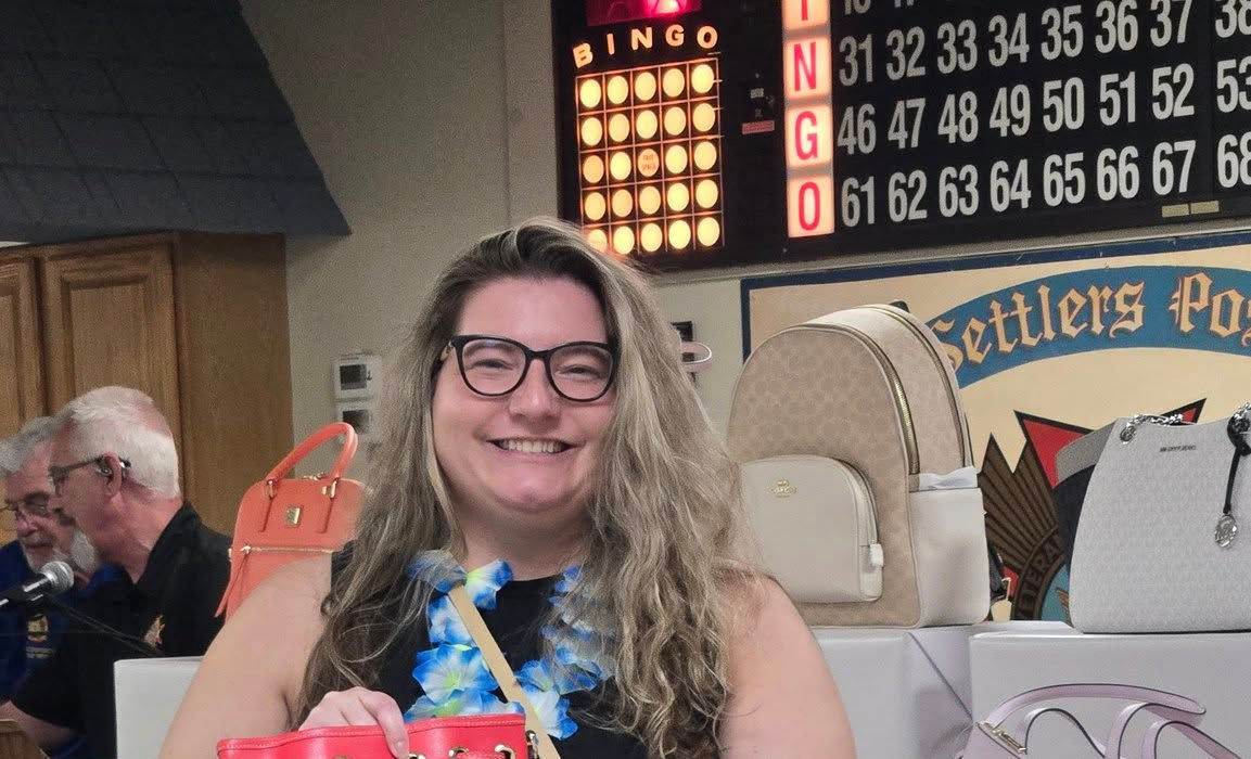 Woman smiling holding a coral colored purse she won.