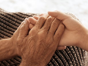 Two hands clasping each other gently over a striped fabric, depicting comfort and support. The setting is soft and neutral in color.