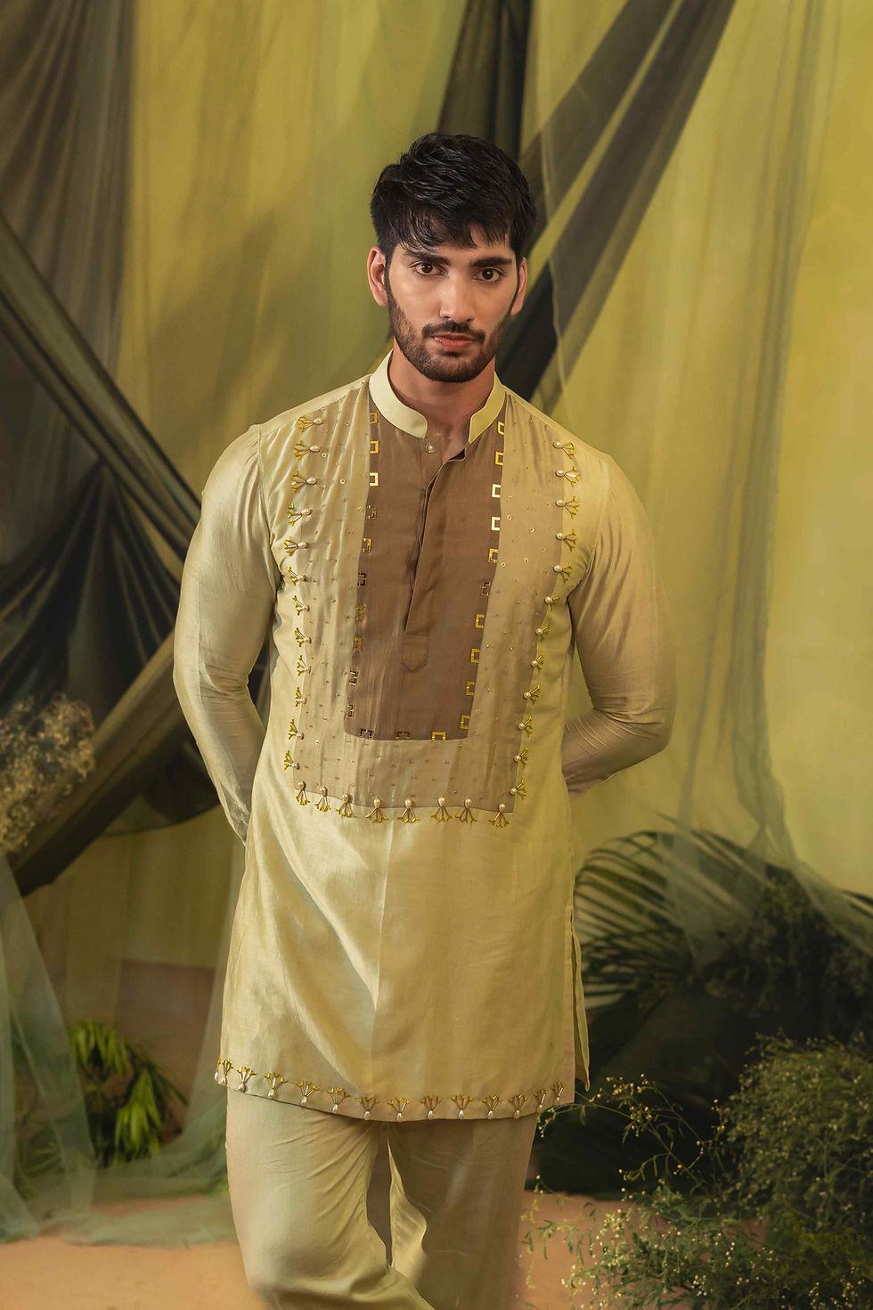 Thumbnail: A person stands in a garden setting, wearing a light green traditional short kurta online with intricate embroidery and gold