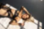 Blonde woman laying in dramatic sunlight, wearing black lingerie, staring into the camera - Northampton boudoir
