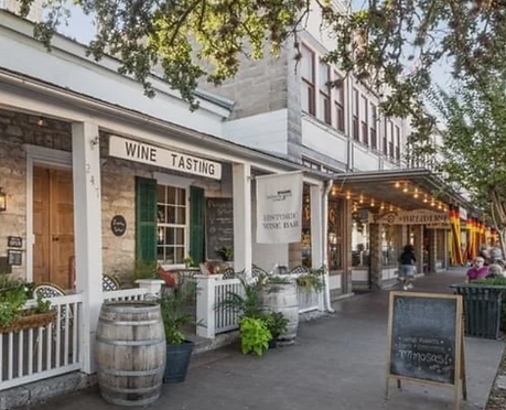 Cute row of shops in downtown Marble Falls near Talula Mesa Glamping resort. A sign in the foreground reads "wine tasting" outside of Cuvee wine and piano bar.