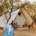 Beautiful Christmas glamping tent in the hill country near Austin, TX. Woman with cozy blanket running to her unique glamping tent overlooking Lake Travis near Marble Falls, Texas. Tent is beautifully decorated for Christmas glamping with a Christmas wreath and poinsettias.