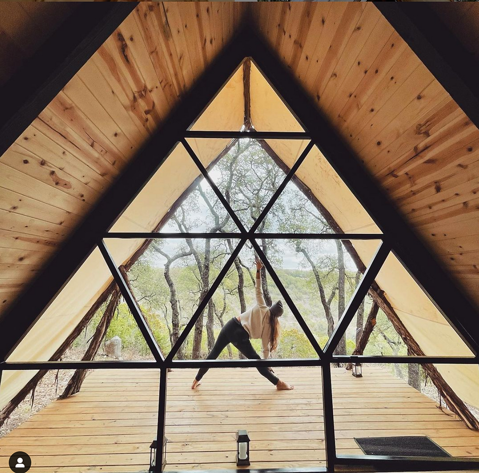 Gorgeous glamping near Austin, Texas. Talula Mesa glamping tent or dome, with a woman doing yoga on the back porch overlooking Lake Travis and the Texas hill country, next to a giant glass wall and covered porch.