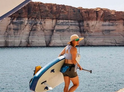 Glamping guest, a woman, carrying a paddleboard and paddle next to Lake Travis near Austin, TX