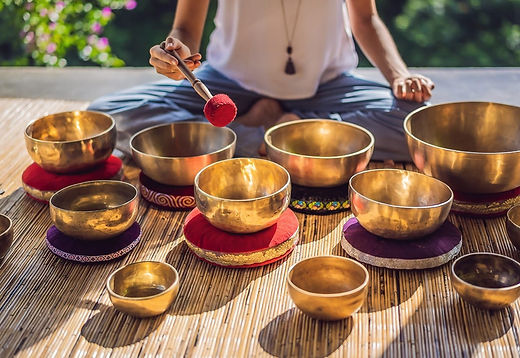 Sound bath near Austin TX in the hill country. An instructor sits in front of a dozen brass signing bowls on a bamboo mat in the sun.