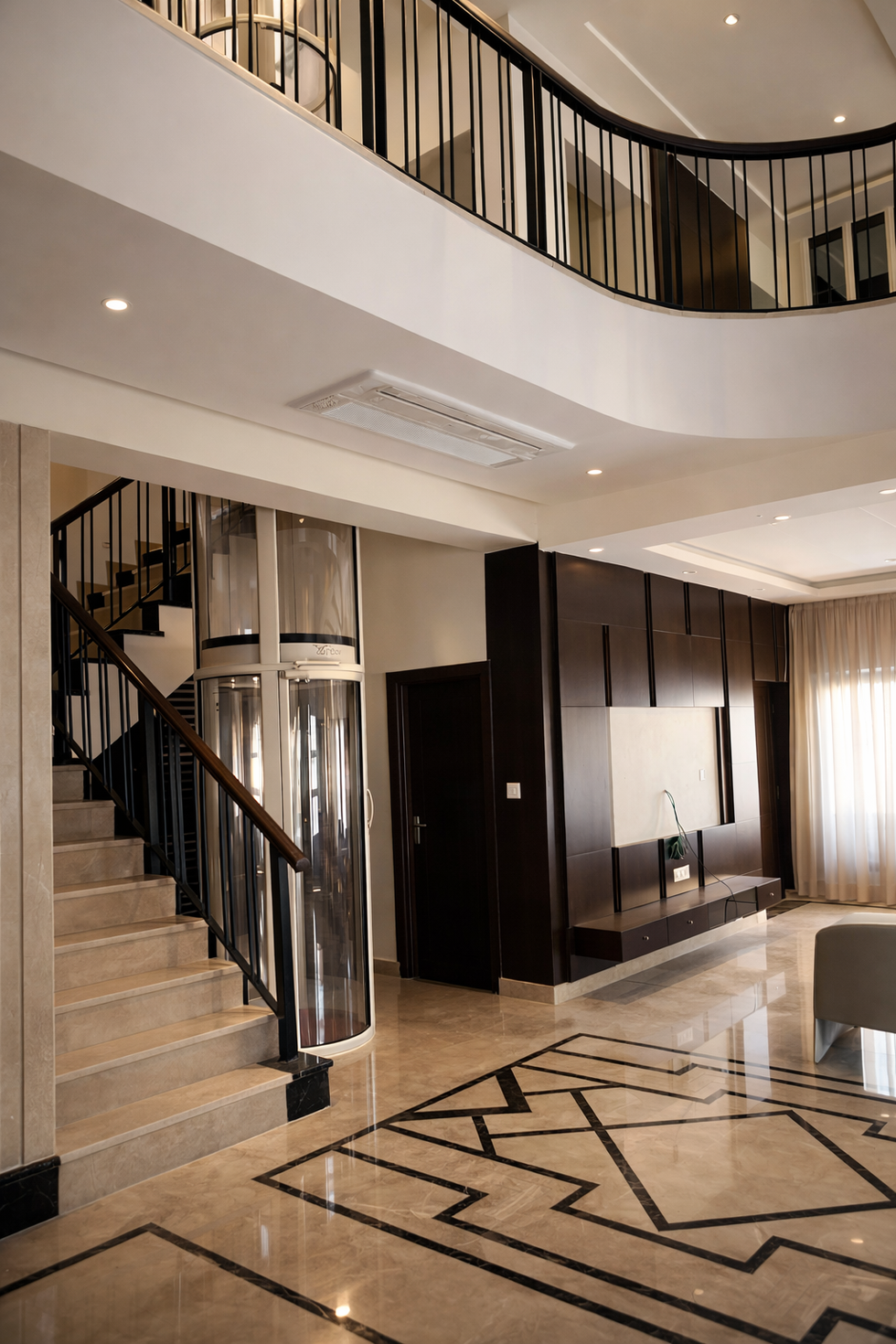 Elegant staircase with integrated glass elevator and dark wood feature wall in a contemporary luxury villa interior.