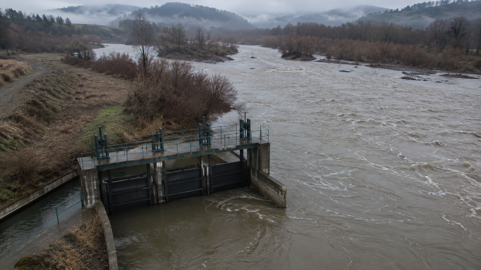 Vista aérea editorial de una bocatoma chilena con compuertas cerradas por resolución DGA sobre río en crecida invernal — cumplimiento de la orden preventiva vigente entre mayo y septiembre 2026